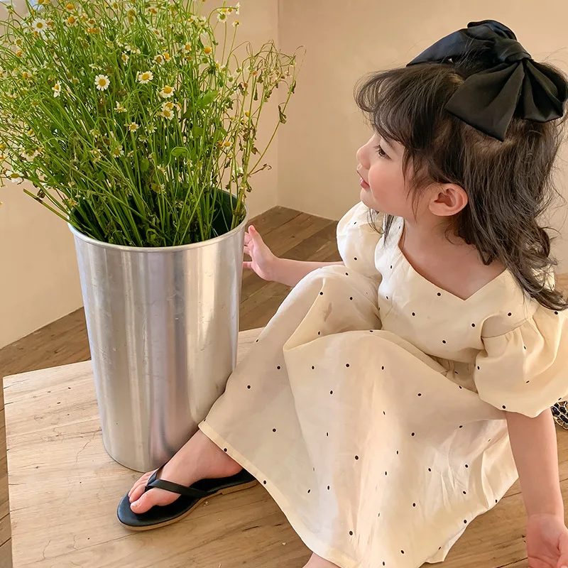 Child seated in the white dotted dress, showing the flowing skirt and puff sleeves.