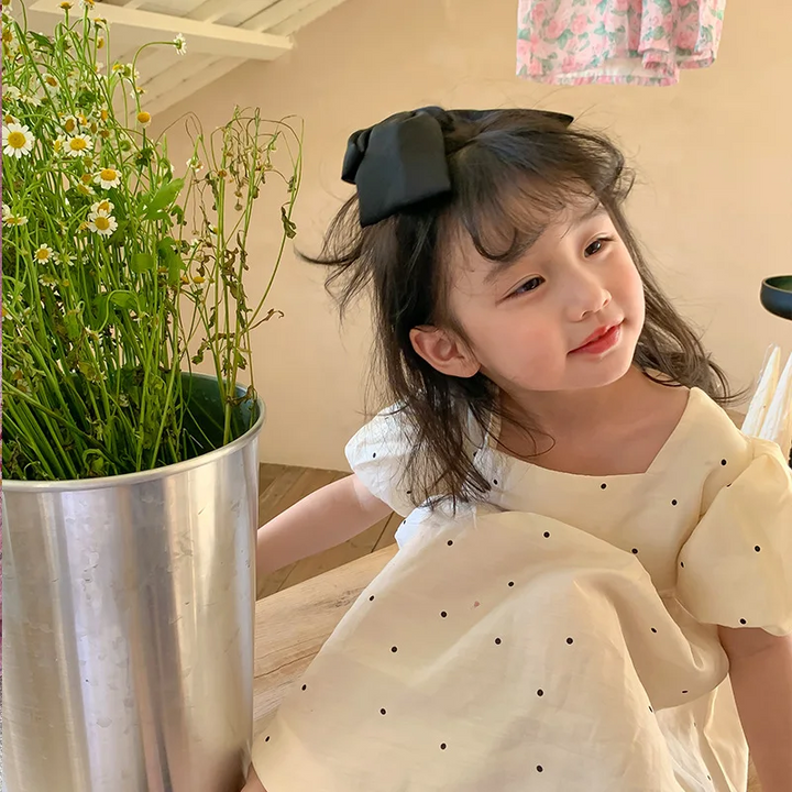 Close front view of a child wearing the dotted dress, showing its neckline and puff sleeves.