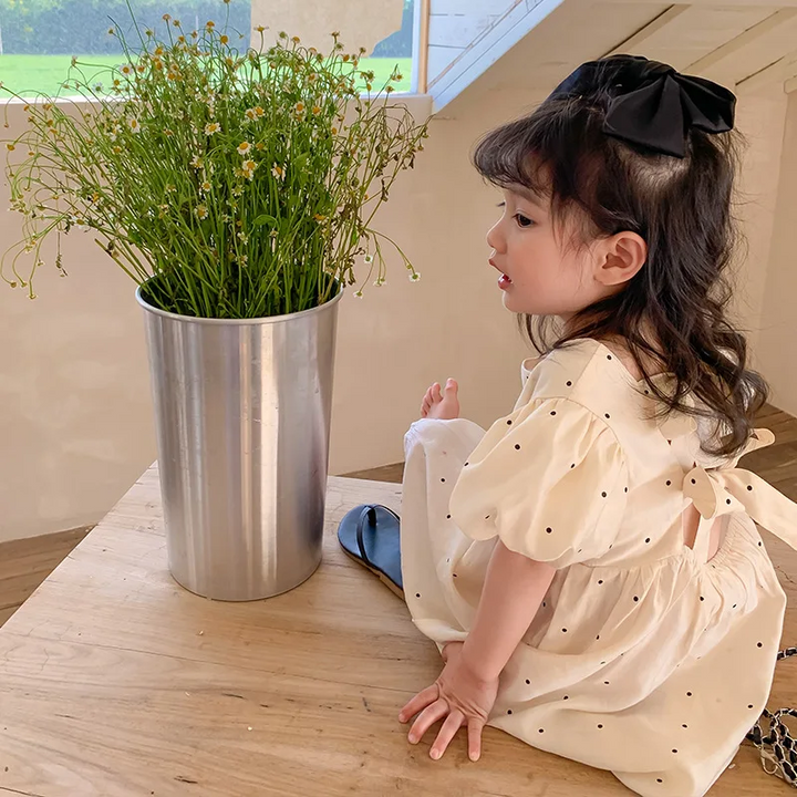 Side and back view of a child wearing the dotted puff-sleeve dress while seated on a table.