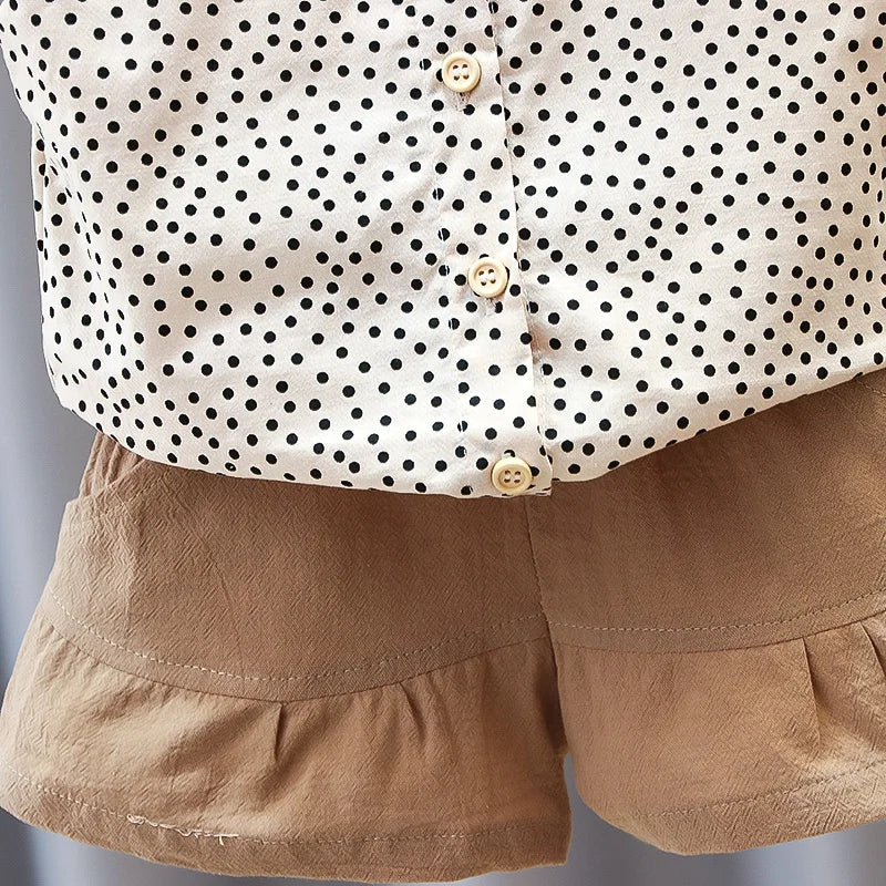 Lower button-front detail of the dotted top above tan ruffle-hem shorts