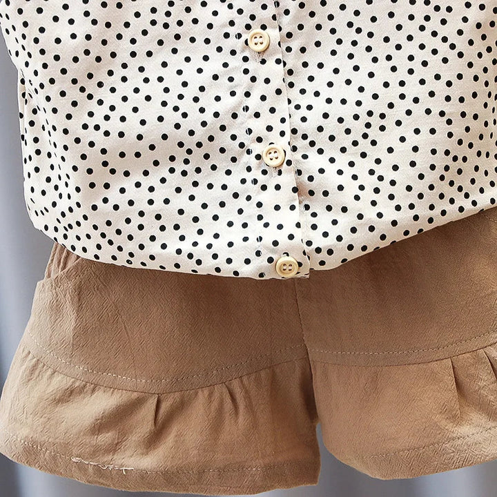 Lower button-front detail of the dotted top above tan ruffle-hem shorts