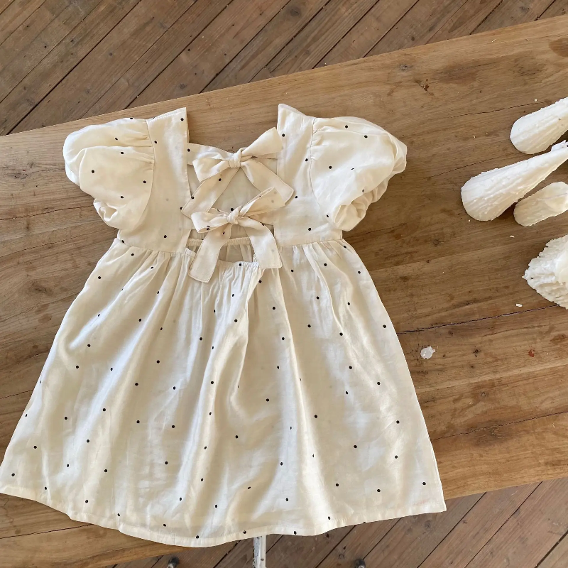 Back view of the white dotted dress laid flat, showing two fabric bows and the A-line skirt.
