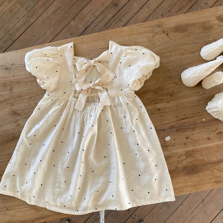 Back view of the white dotted dress laid flat, showing two fabric bows and the A-line skirt.