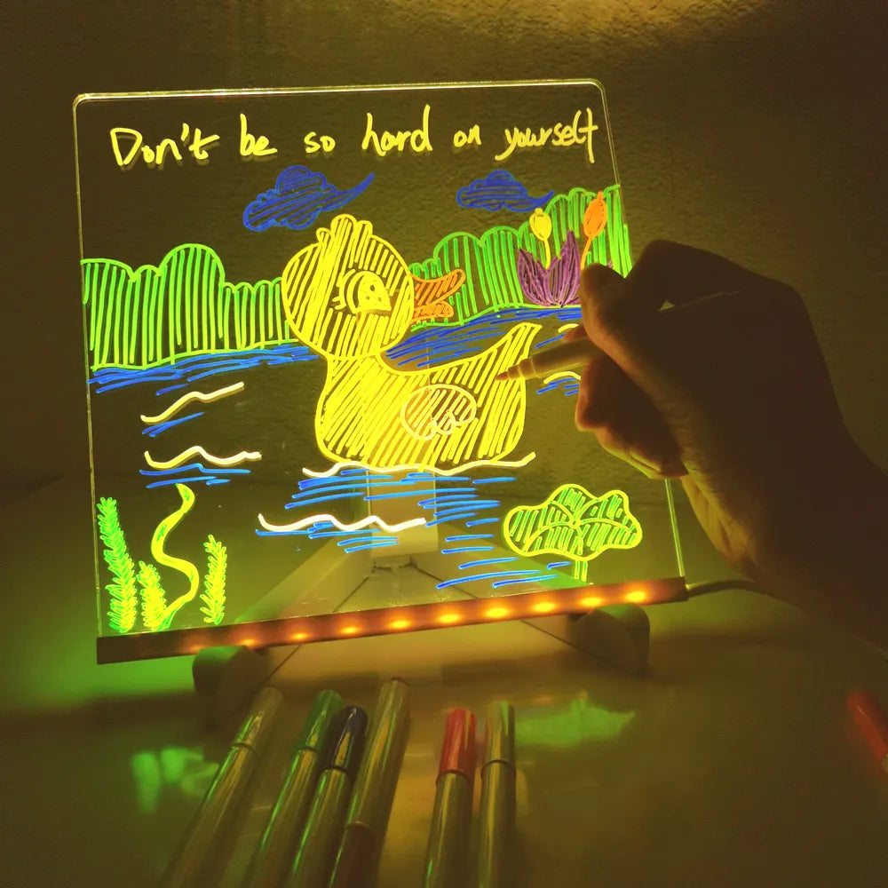 Hand adding colorful details to a duck drawing on an illuminated board, with pens in front