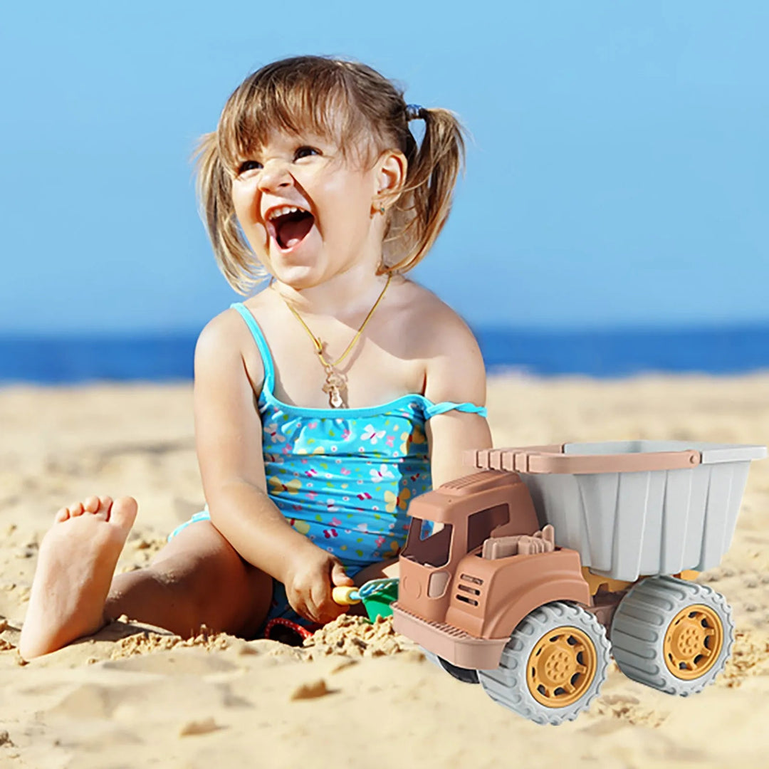 Child sitting on the beach beside a toy dump truck with a gray bed