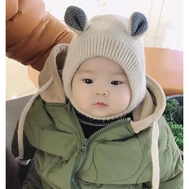 Baby wearing a beige ear-topped balaclava with a green winter jacket