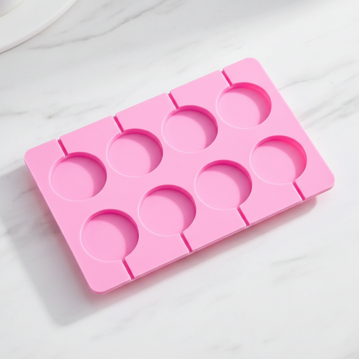 Pink silicone lollipop mold with eight round cavities on a marble surface
