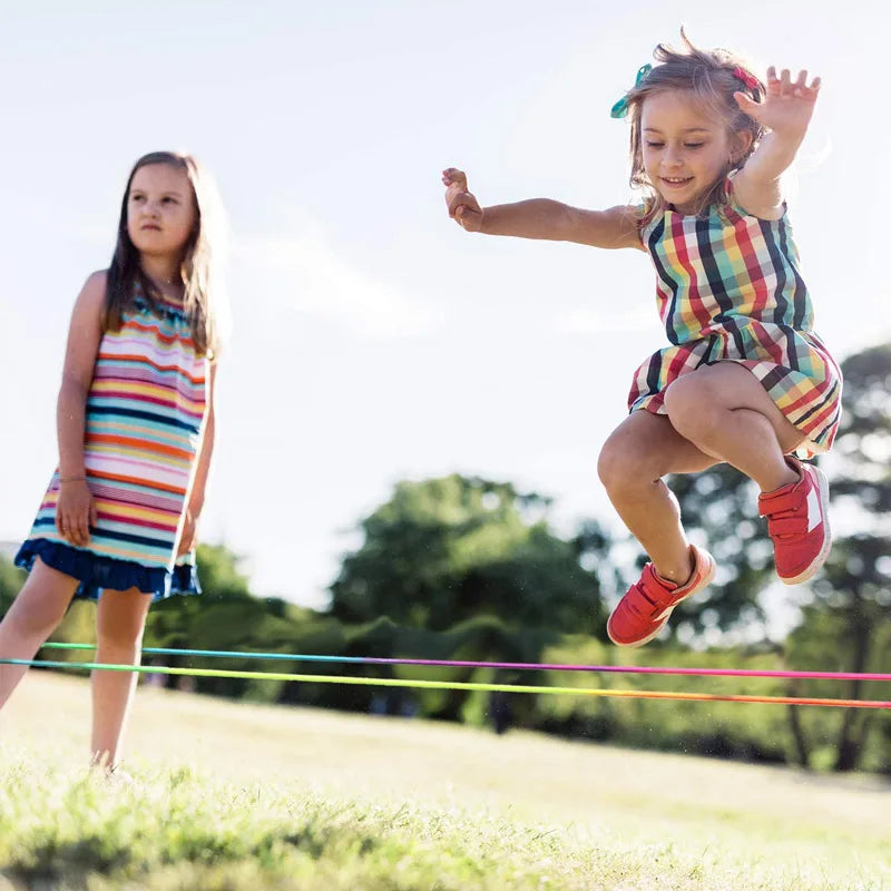 Girl jumping over a multicolor elastic band on the grass