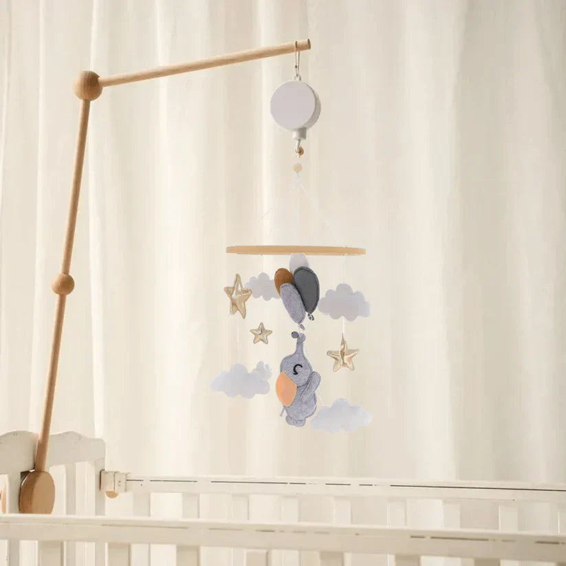 Elephant-and-balloon baby mobile hanging from a wooden mounting arm above a white crib
