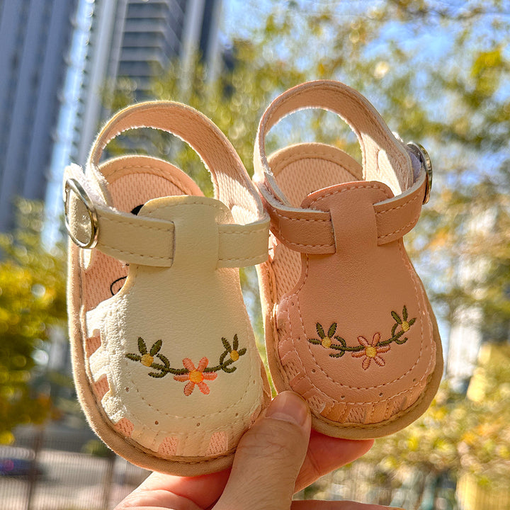 Floral baby sandals held outdoors in sunlight, showing embroidered fronts and adjustable straps