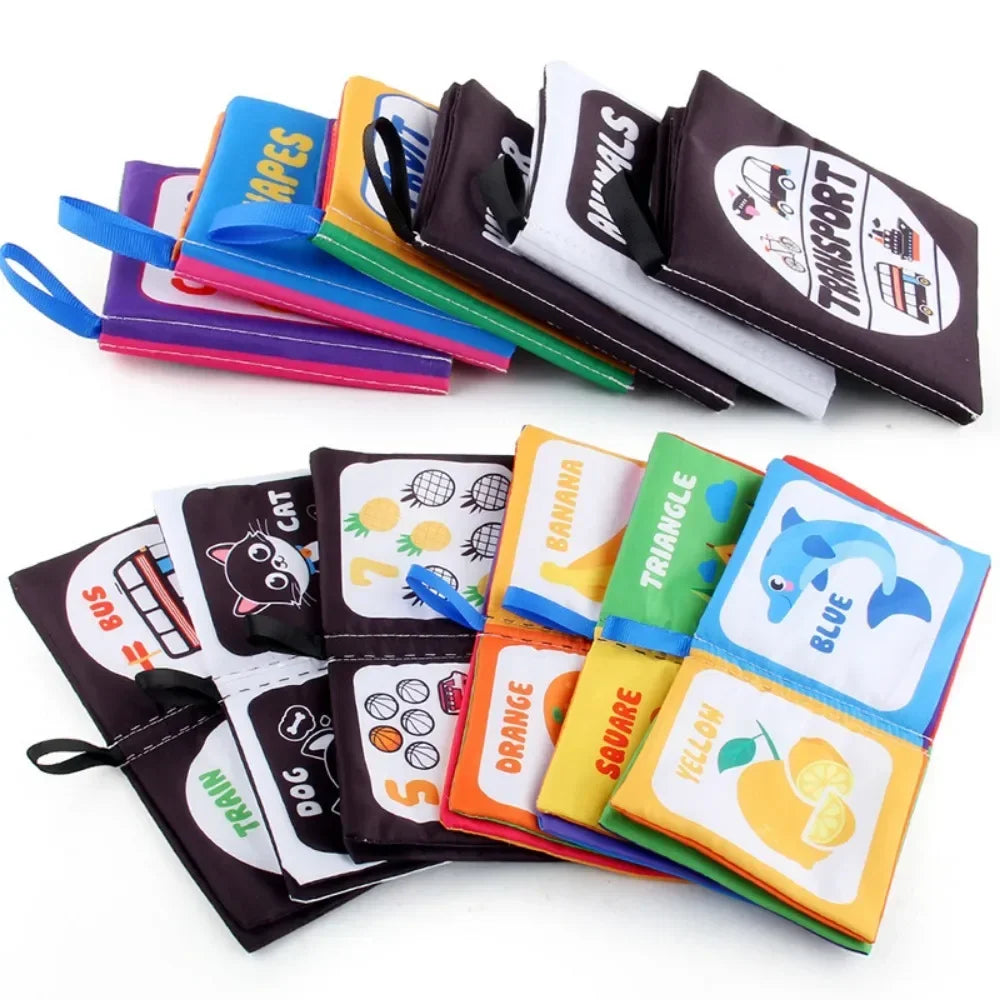 Stacked fabric activity books with open pages showing colors, shapes, animals and vehicles