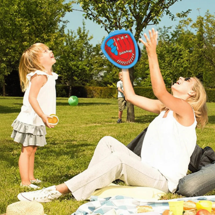 Adult and child playing catch with a blue paddle beside a picnic blanket