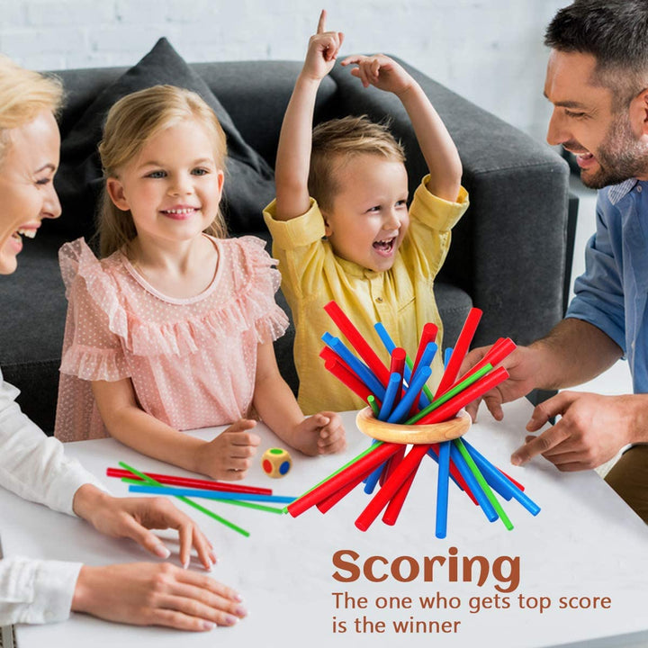 Children and adults gathered around a wooden stick-balancing game on a table.