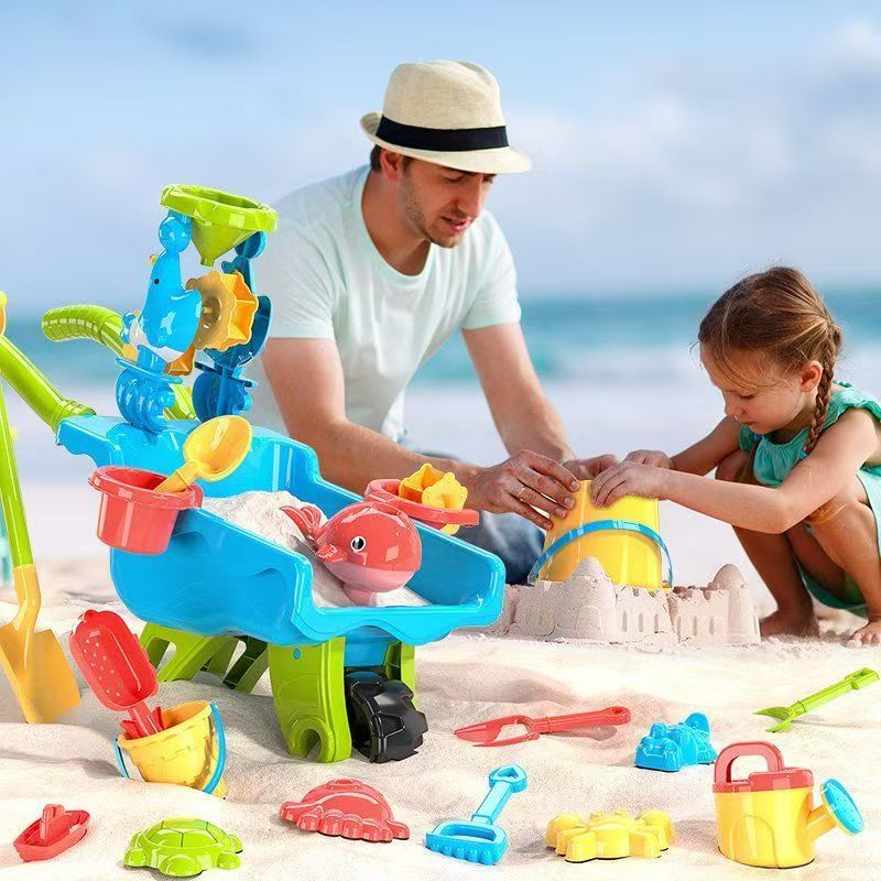 Adult and child building sandcastles beside a blue toy wheelbarrow and colorful sand tools