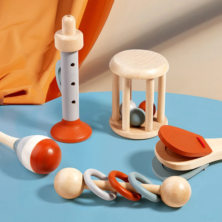 Five wooden musical toys on a blue tabletop, including rattles, a maraca, clapper and recorder-style toy