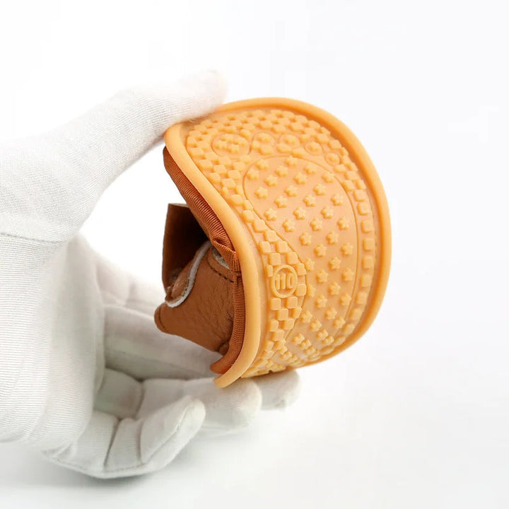 Brown baby sandal bent to show its flexible sole and textured orange tread