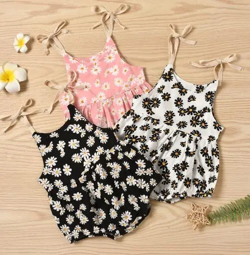 Black, pink, and white floral baby rompers with beige shoulder ties on a wooden surface
