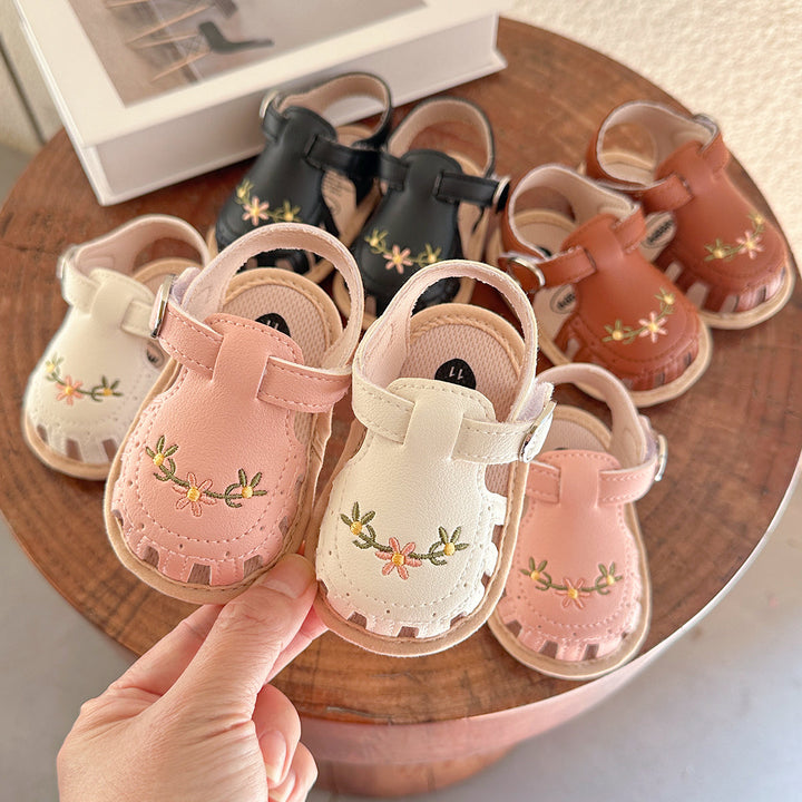 Pink and white floral baby sandals held in front of an assortment on a round wooden table