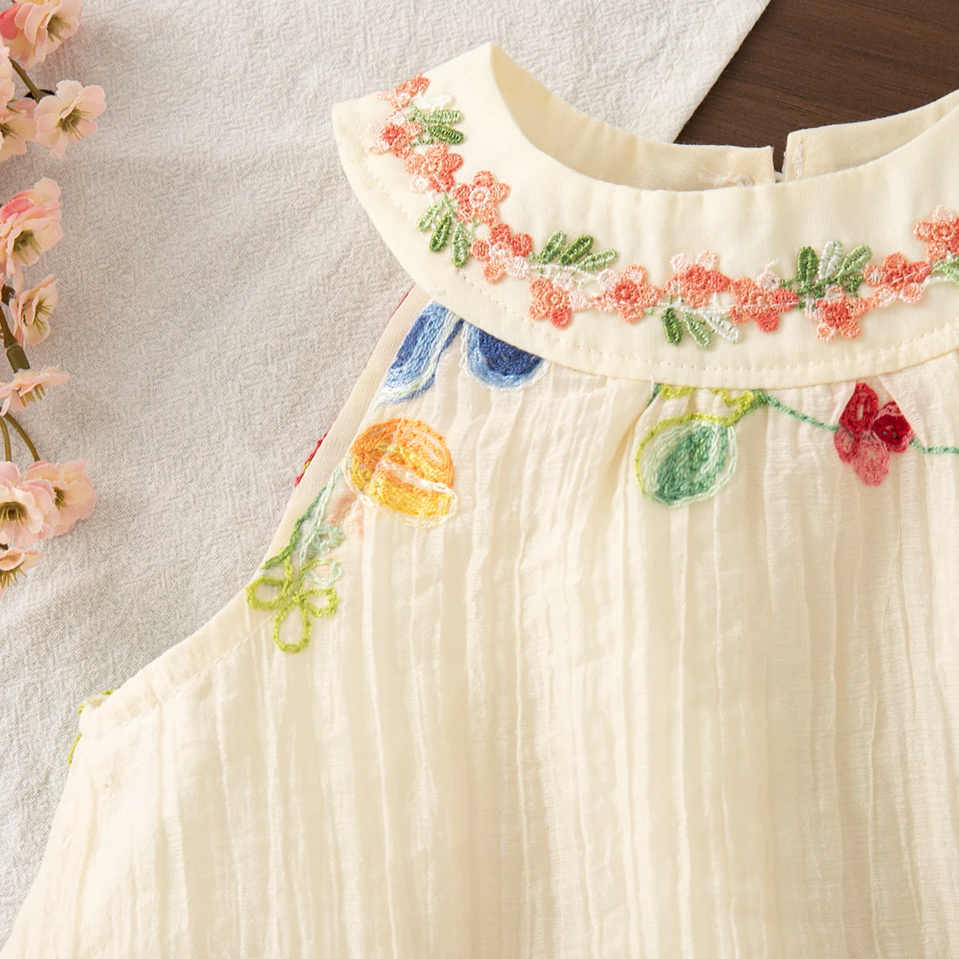 Detail of the embroidered collar, sleeveless armhole, and softly gathered cream fabric