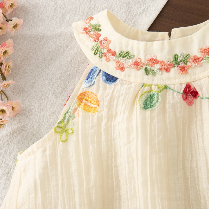 Detail of the embroidered collar, sleeveless armhole, and softly gathered cream fabric
