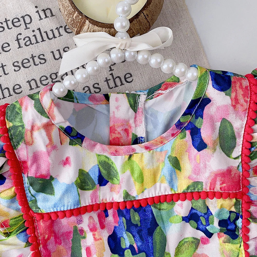 Close-up of the floral dress neckline, ruffled shoulder, and red bobble trim