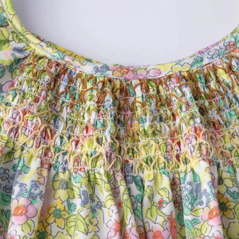 Close-up of elastic smocking and small pink, yellow, and green flowers on the dress bodice.