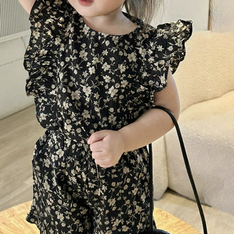 Close-up of the black floral outfit showing layered shoulder ruffles and a gathered waistband
