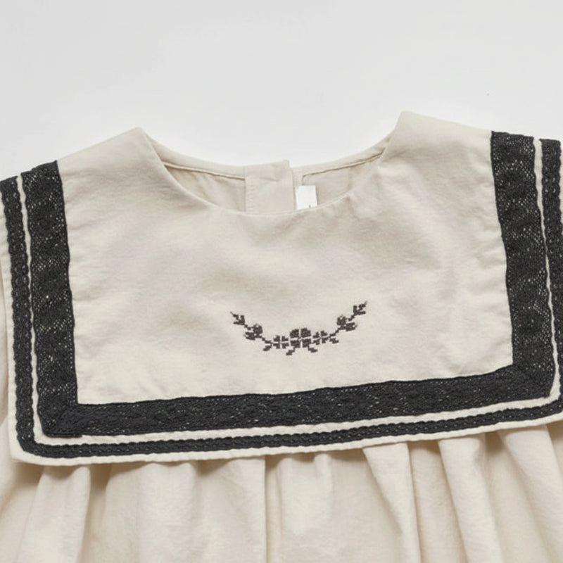 Close-up of floral embroidery and black lace trim on the cream sailor collar