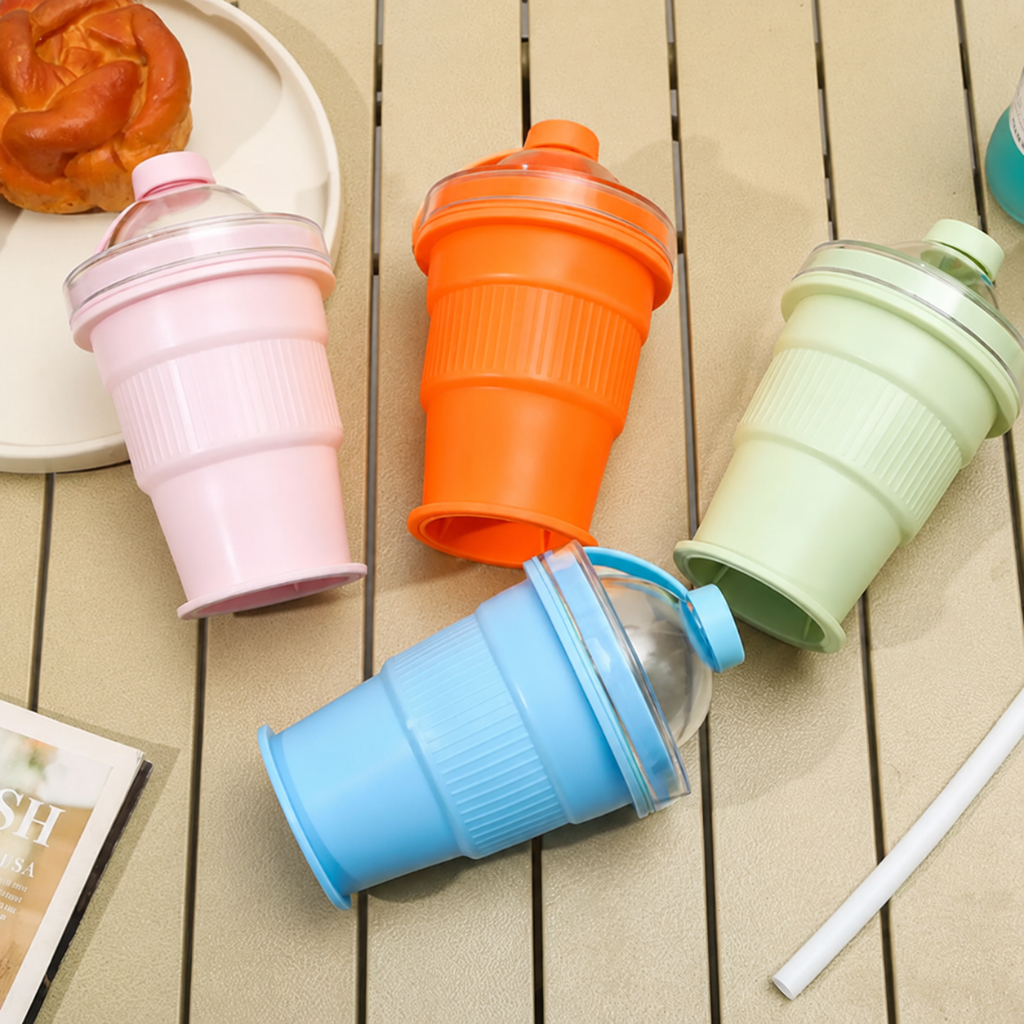 Blue, green, orange, and pink foldable silicone cups with clear domed lids on an outdoor table