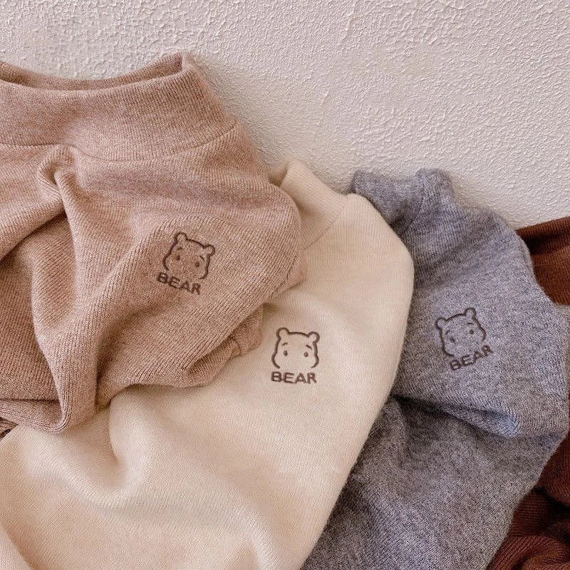 Folded khaki, beige and gray fleece shirts showing ribbed necklines and bear details