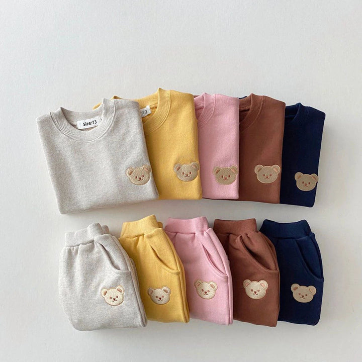 Folded bear-patch sweatshirts and pants in gray, yellow, pink, brown, and navy blue