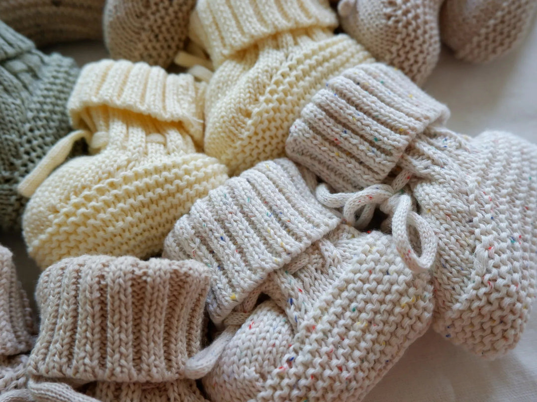 Close-up of neutral and pale yellow baby booties with folded cuffs and tie details.