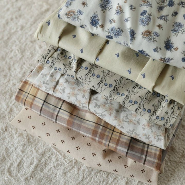 Folded fabrics showing blue floral, small-print, and beige checkered patterns.