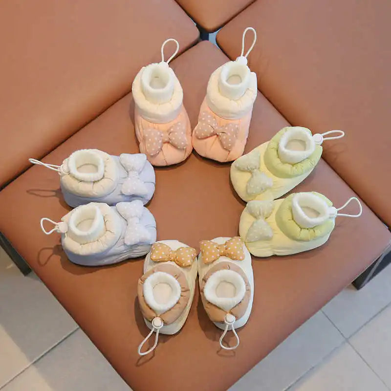 Four pairs of bow baby shoes in pink, pale blue, green, and white arranged on a chair