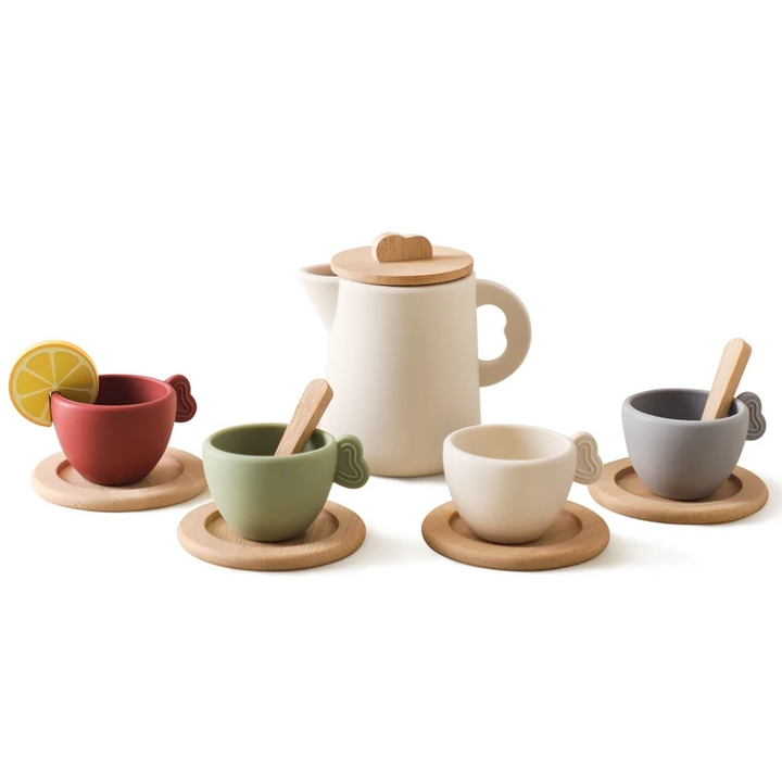 Cream toy teapot with four colored cups, round coasters, spoons, and a pretend lemon slice