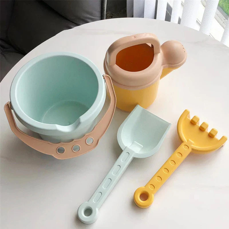 Four-piece beach set with a blue bucket, yellow watering can, shovel, and rake