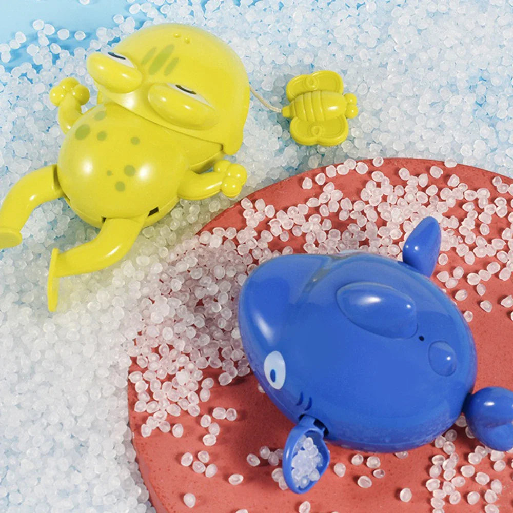 Green frog and blue sea-animal bath toys resting among white granules