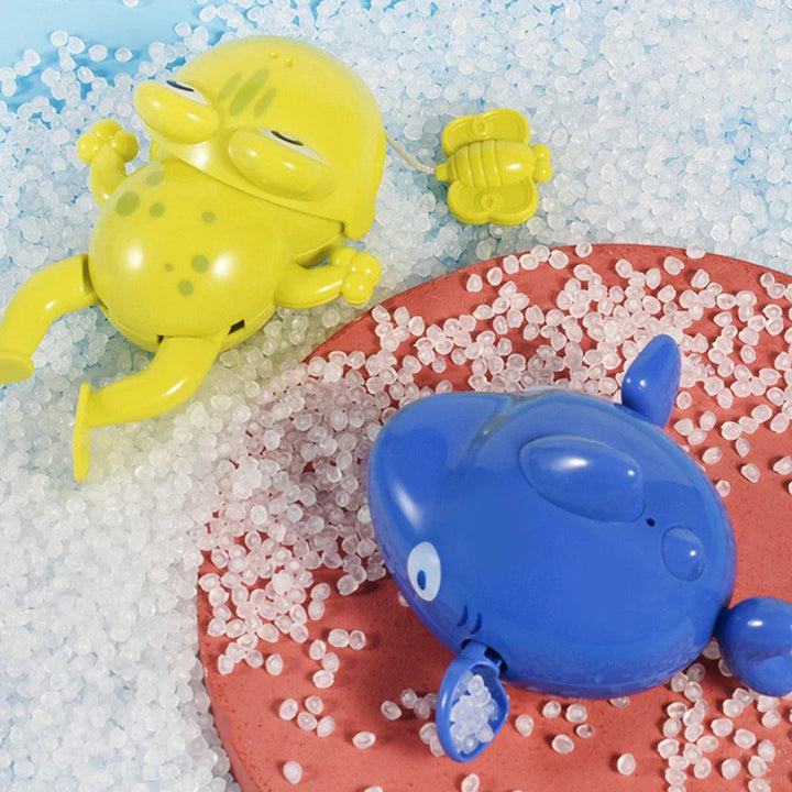 Green frog and blue sea-animal bath toys resting among white granules