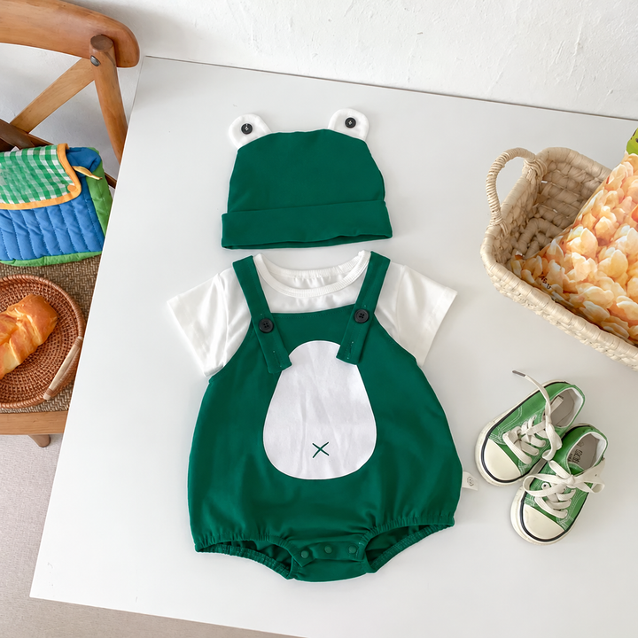 Green frog romper, white short-sleeve top and frog-eye cap in a flat-lay outfit display