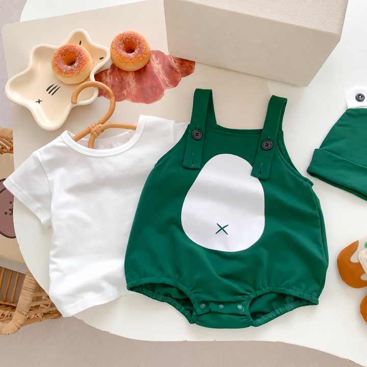 Green frog romper laid beside a white short-sleeve top and green cap