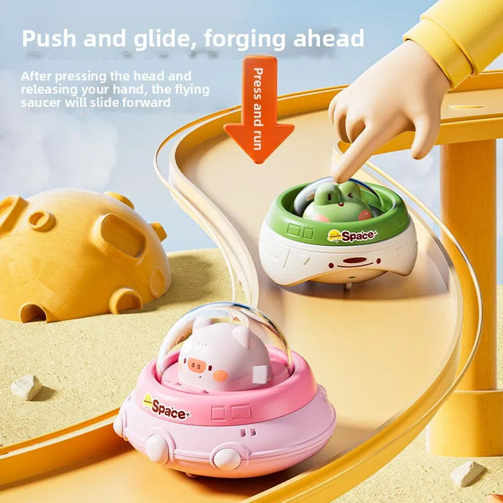 A finger presses the frog pilot on a UFO toy, with a pink UFO farther down the curved ramp.