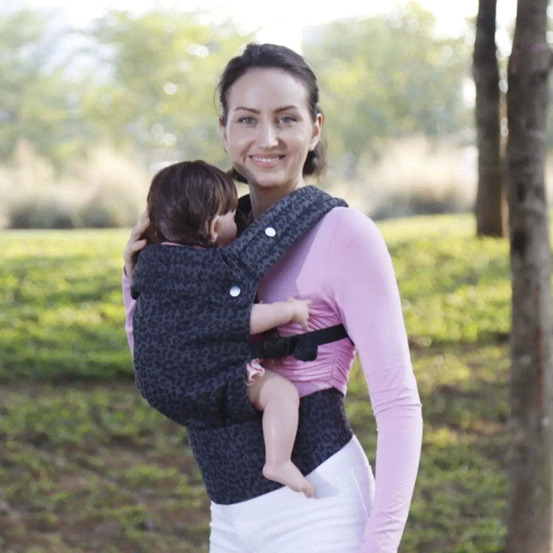 Parent facing the camera while carrying a baby in a dark leopard-print carrier outdoors