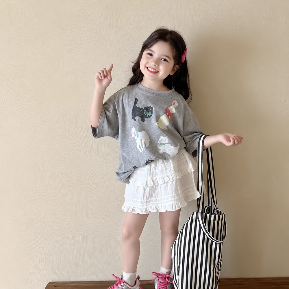 Girl wearing a gray cat-print T-shirt with a white ruffled skirt and holding a striped tote.