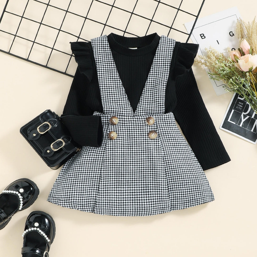 Black ruffle-shoulder top with a black-and-white houndstooth pinafore skirt and four decorative buttons.