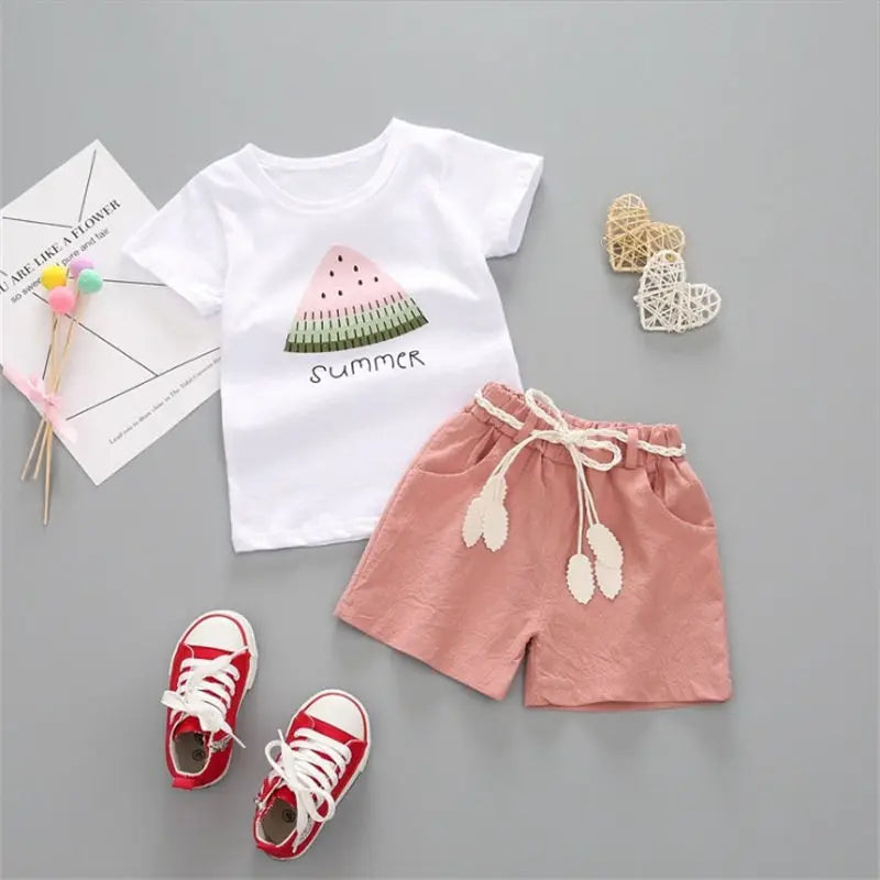 Pink summer shorts and a white watermelon-print tee laid out separately