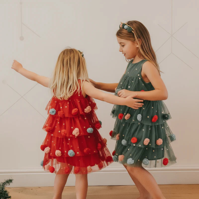 Two girls wearing red and green Christmas dresses with tiered skirts and colorful pom-pom details
