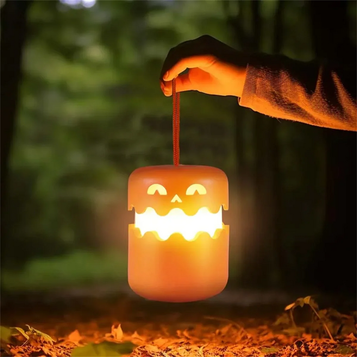 Hand holding a glowing orange pumpkin lantern by its cord outdoors
