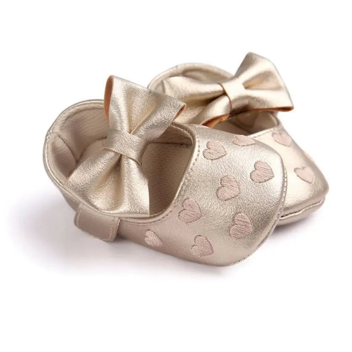 Gold baby shoes with large bows and heart details, shown from the side