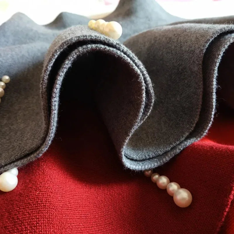 Close-up of folded gray knit fabric over a red skirt with pearl-style bead details