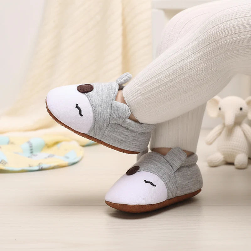 Gray and white animal-face baby shoes worn with ribbed cream pants.
